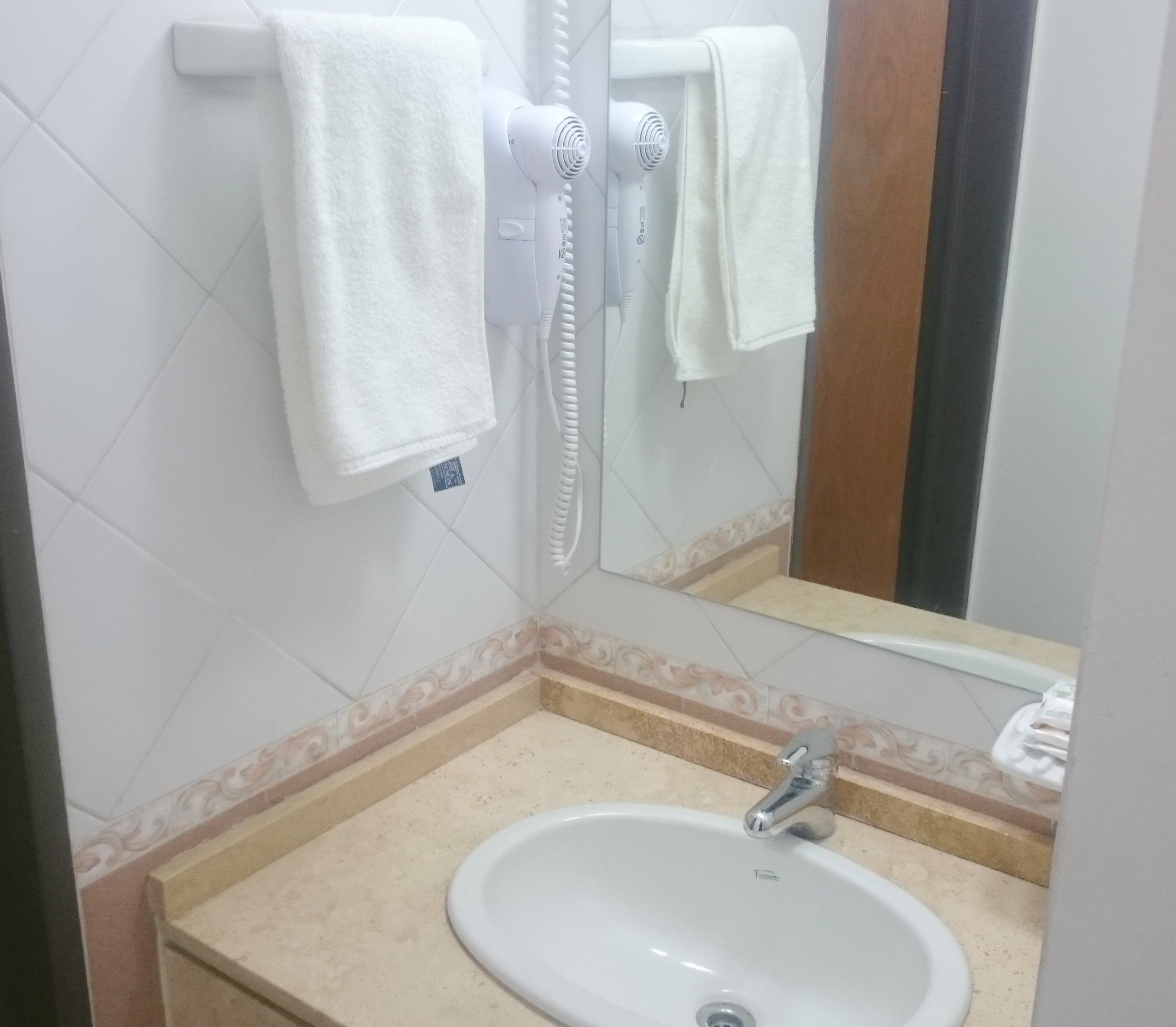 Un baño con lavamanos blanco, un espejo y toallero.