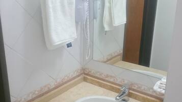 Un baño con lavamanos blanco, un espejo y toallero.