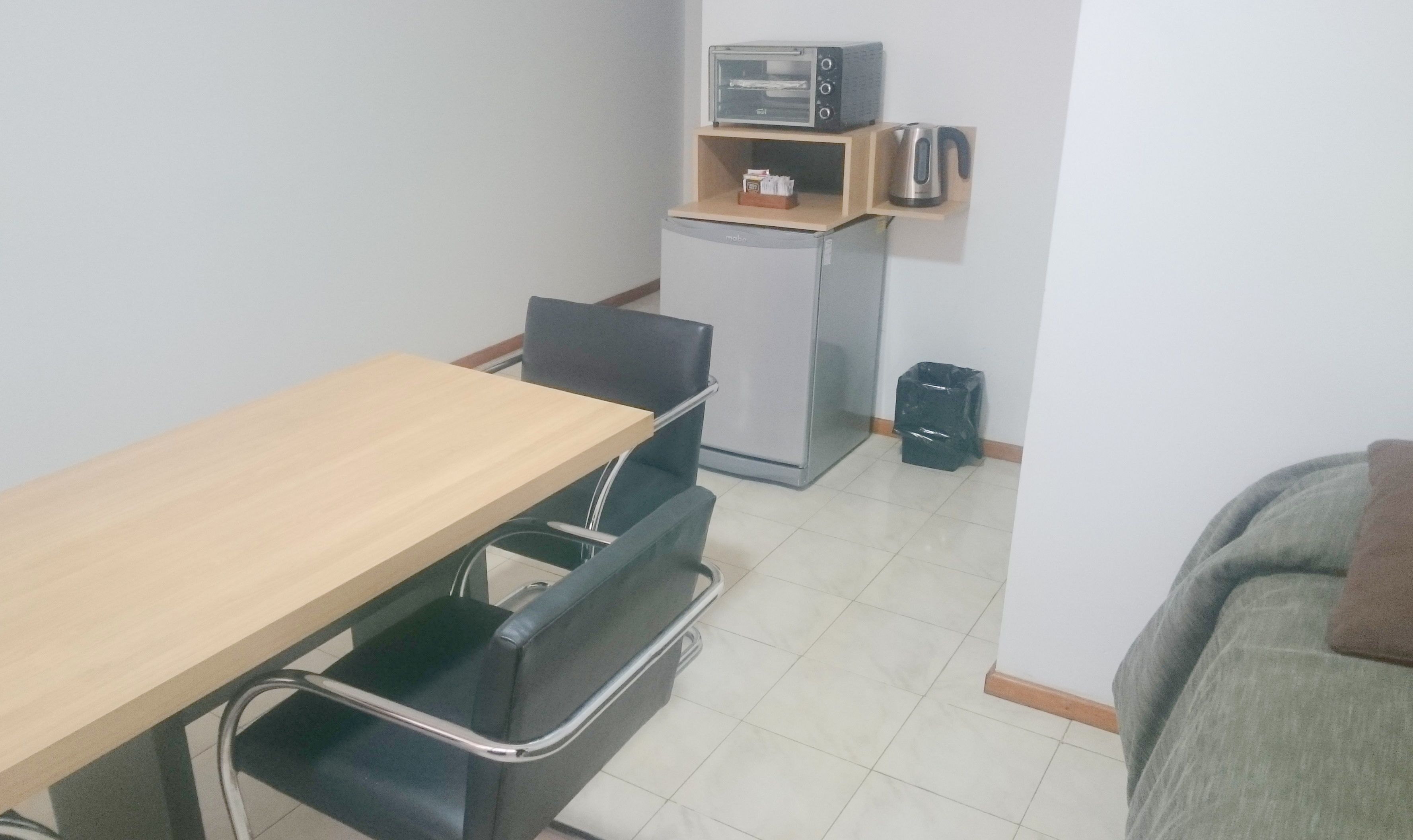 A small kitchenette with a toaster, a refrigerator, and a coffee maker on a shelf.