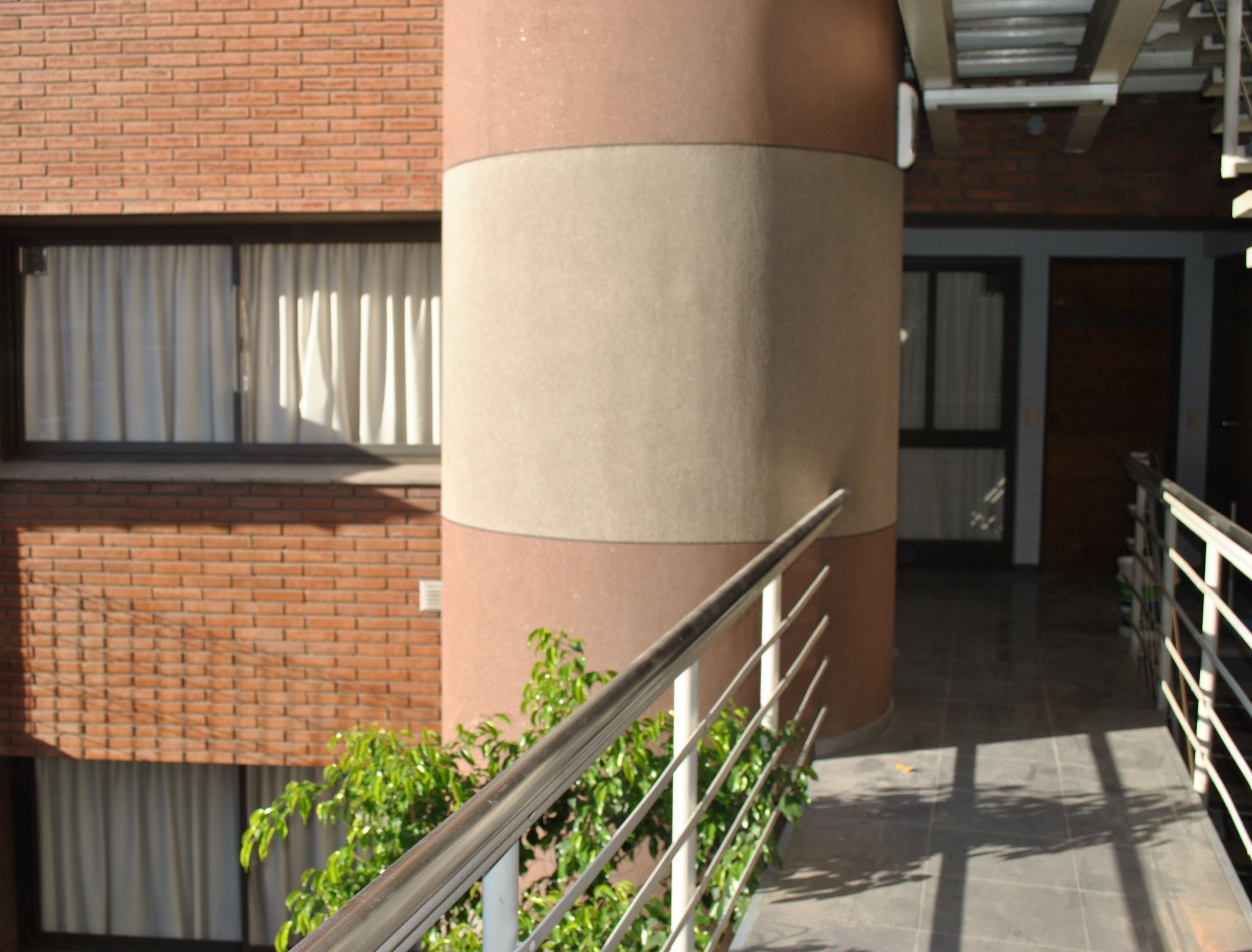 A building exterior with a brick facade, a beige cylindrical column, and a metal railing.