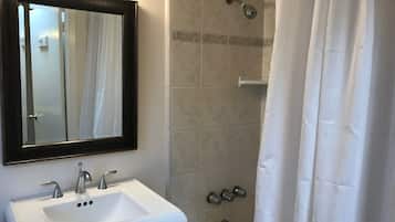 Un baño con lavamanos blanco, un espejo, ducha con cabezal de ducha manual y cortina de ducha blanca.
