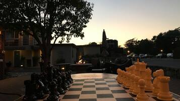 A chessboard set up outdoors with a tree and a building in the background.