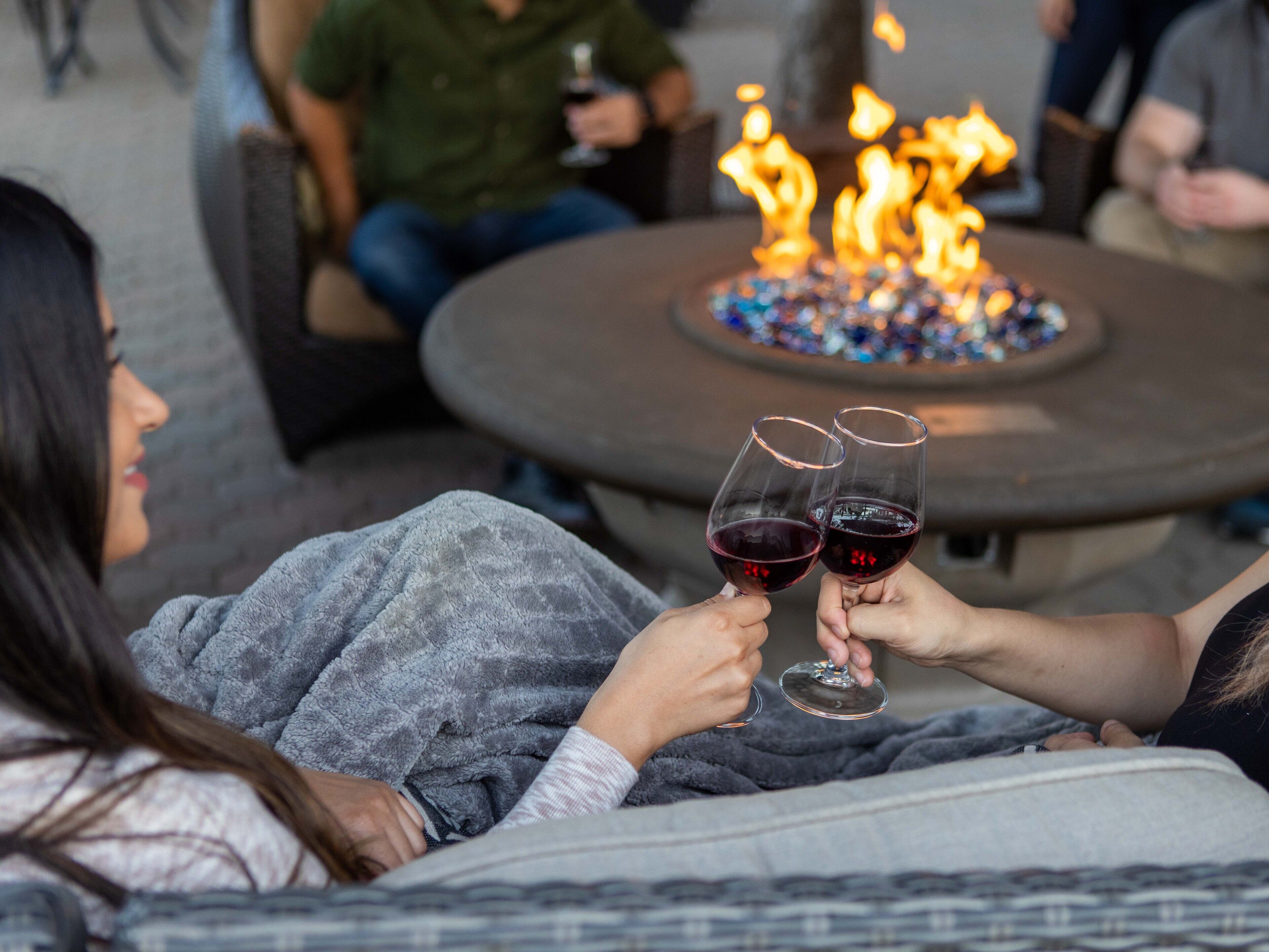Un grupo de personas sentadas alrededor de una mesa redonda con una chimenea, sosteniendo copas de vino.