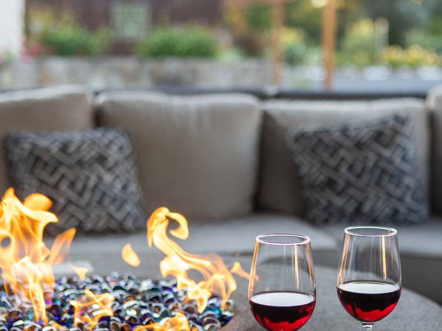 Un foyer avec des galets de verre et deux verres de vin rouge posés sur une surface texturée, avec un espace extérieur flou en arrière-plan.