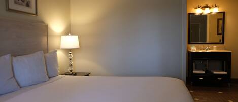 Een hotelkamer met een groot bed, een bedlampje, een ingelijst kunstwerk aan de muur, en een badkamer met een spiegel en wastafel.