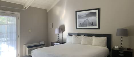 A bedroom with a large bed, a ceiling fan, a framed picture on the wall, and a nightstand with a lamp.