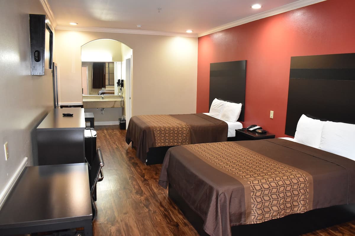 A hotel room with two beds, a desk, a chair, a mirror, and a red accent wall.