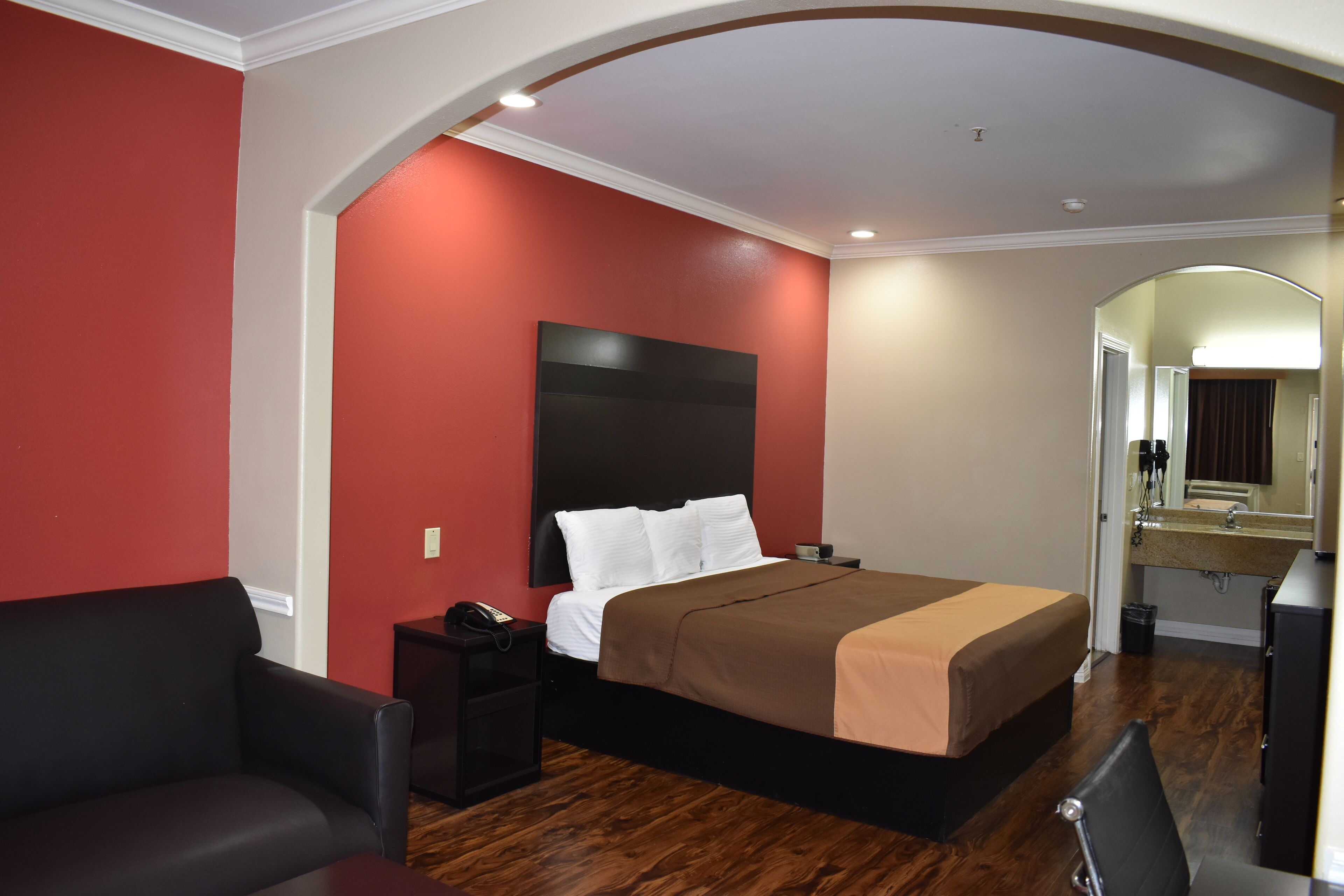 Une chambre d’hôtel avec un grand lit, un fauteuil en cuir noir, une table de chevet avec un téléphone et un plancher en bois.