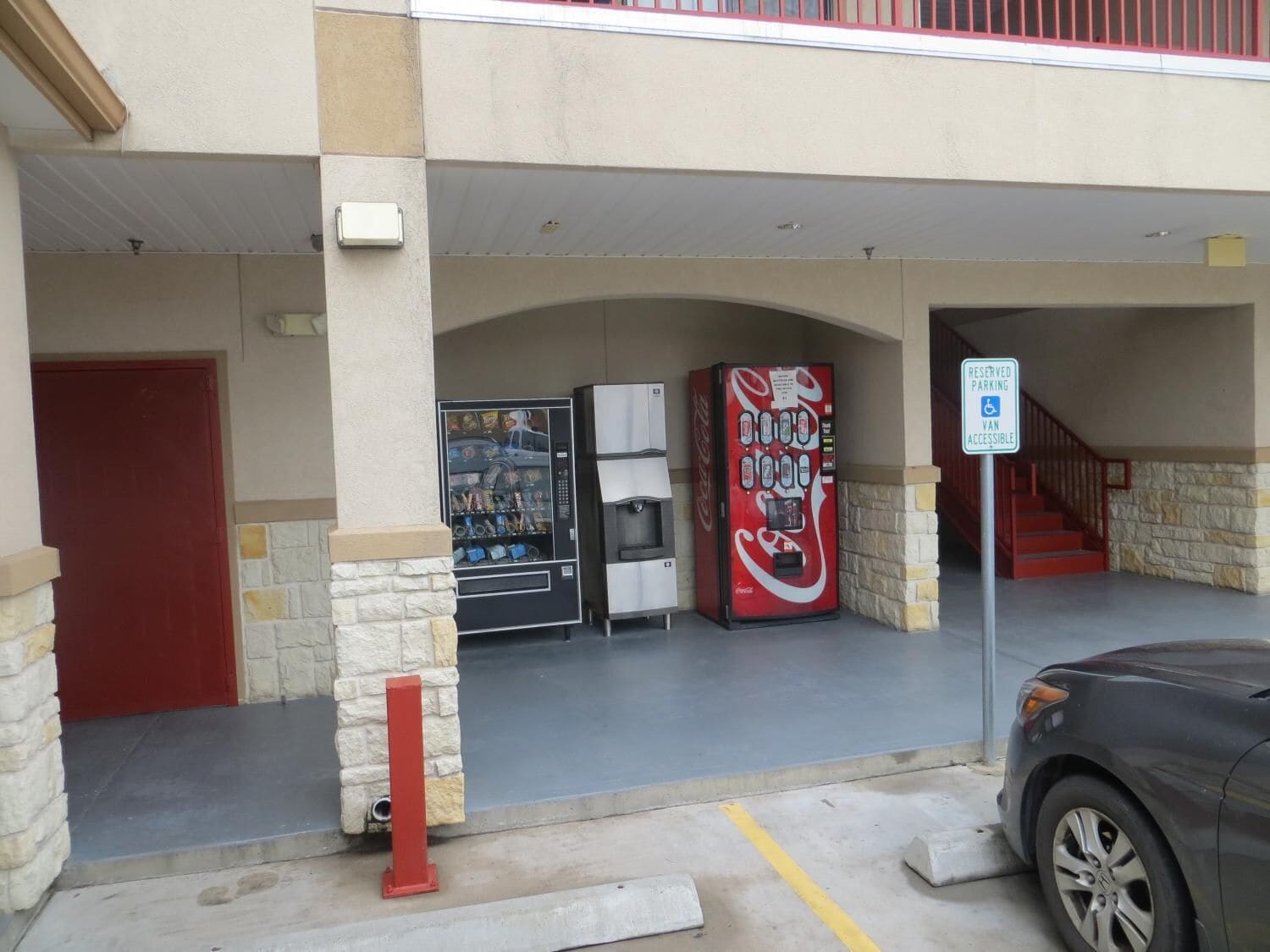 Ein Parkplatz mit einem Schild für reservierte Parkplätze, einer Coca-Cola-Getränkeautomaten und einem Kühlschrank.