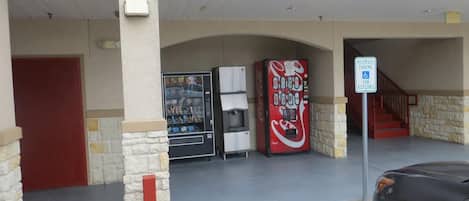Uma área de estacionamento com placa de vaga reservada, uma máquina de refrigerantes Coca-Cola e uma geladeira.