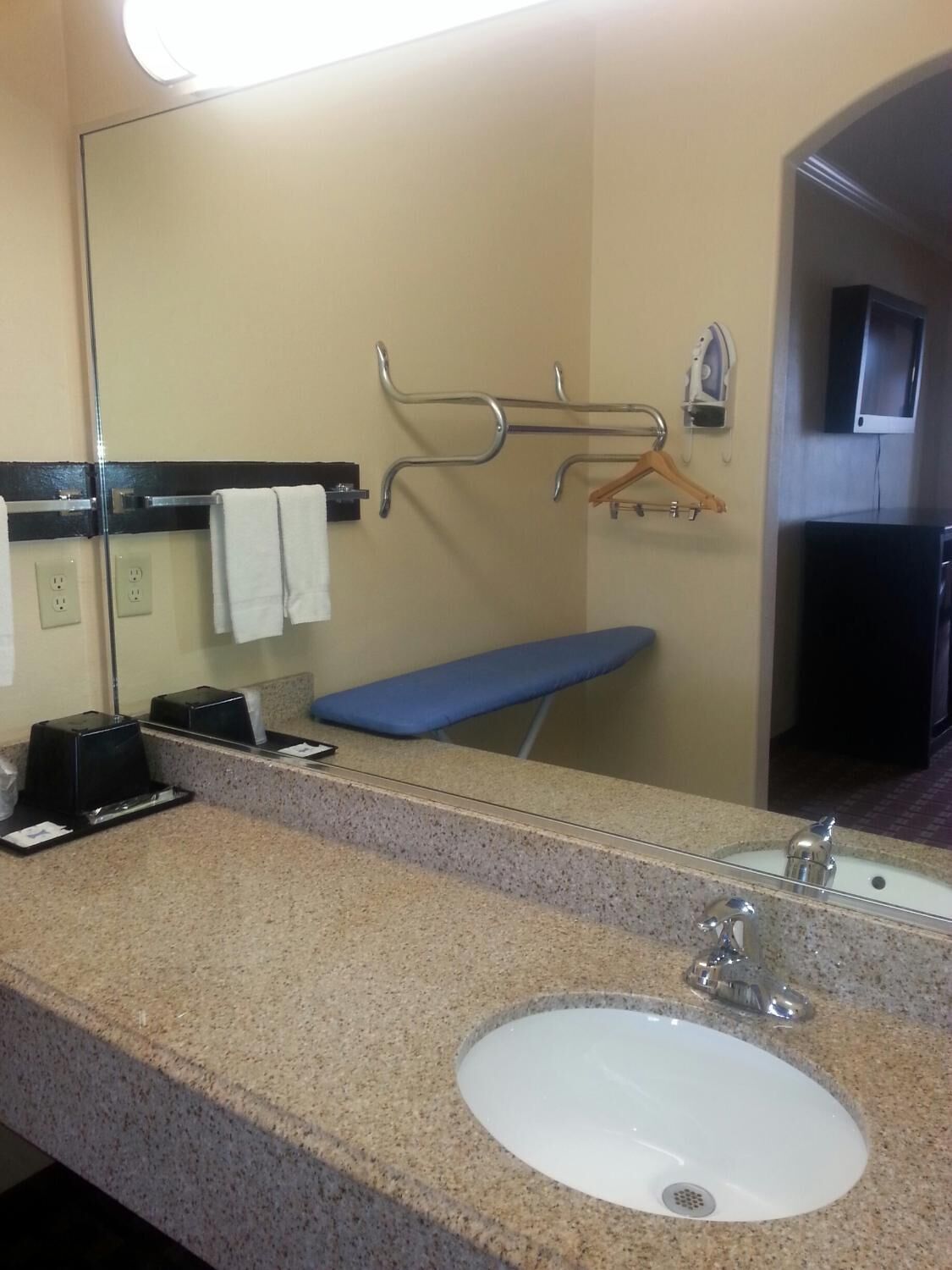 A hotel bathroom with a granite countertop, a sink, a mirror, a towel rack, and a bench.
