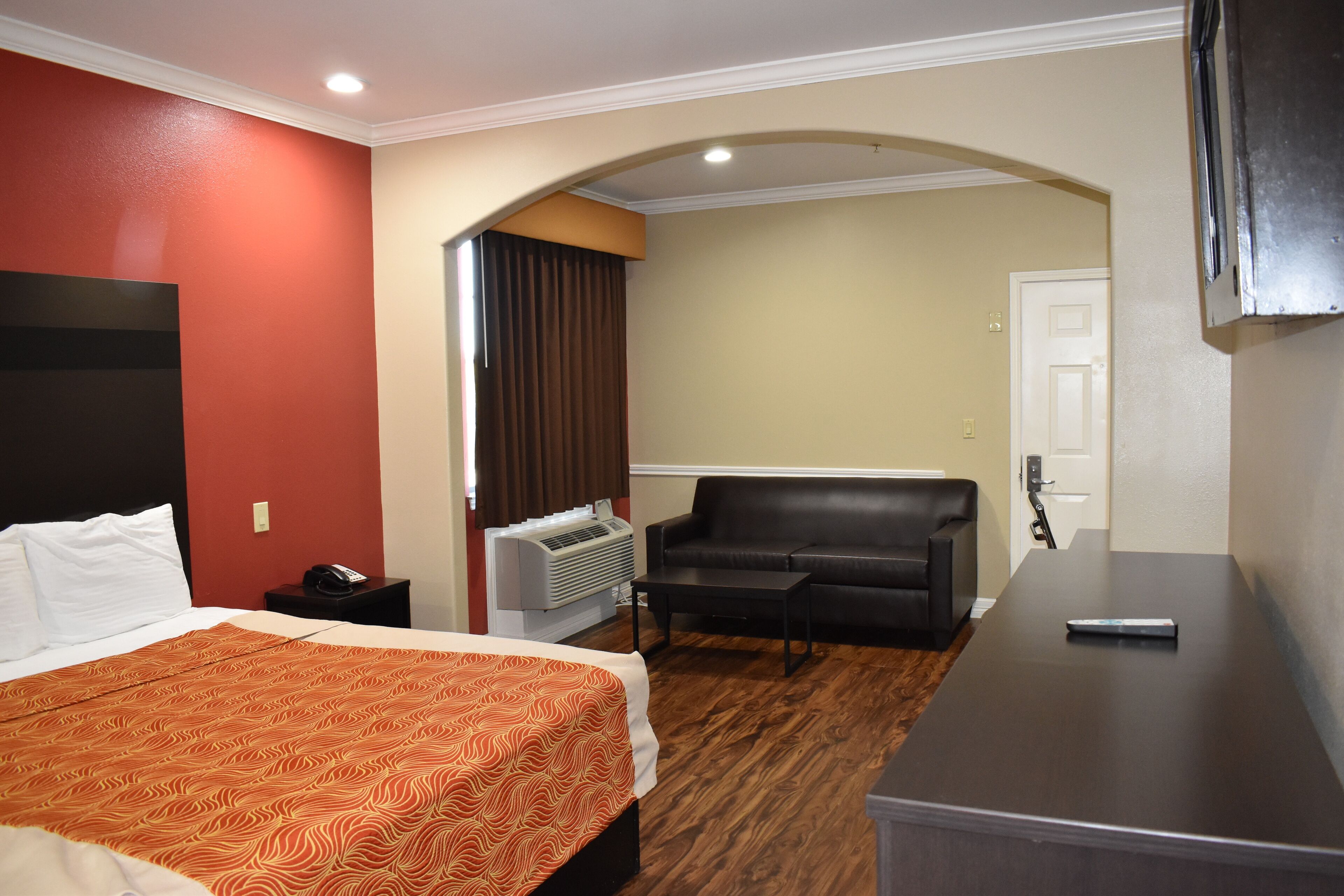 A hotel room with a bed, a desk, a sofa, and an air conditioning unit.