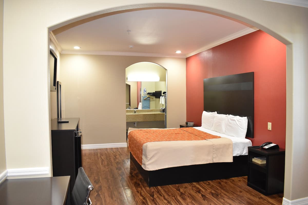 A hotel room with a bed, a nightstand, a desk, and a mirror.