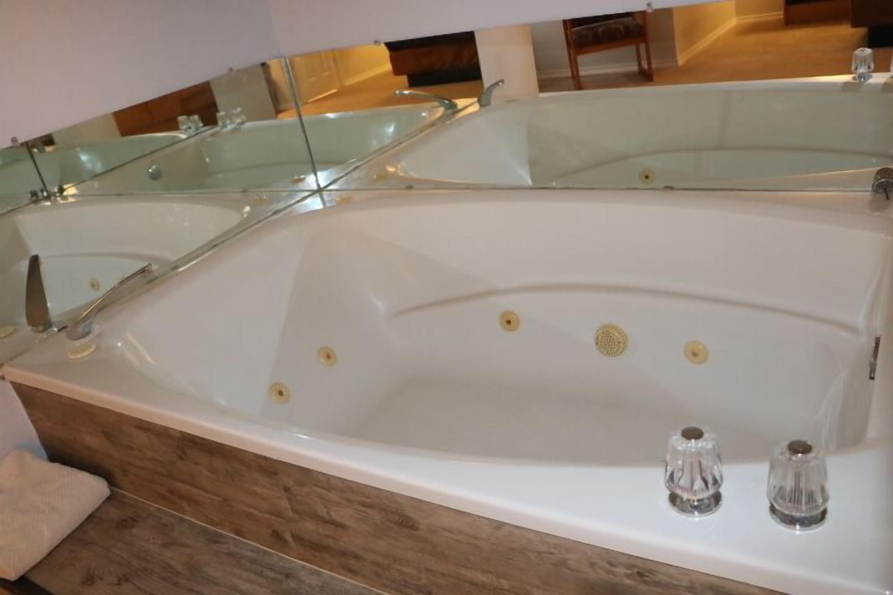 A modern bathroom with a large bathtub, glass shower enclosure, and wooden flooring.