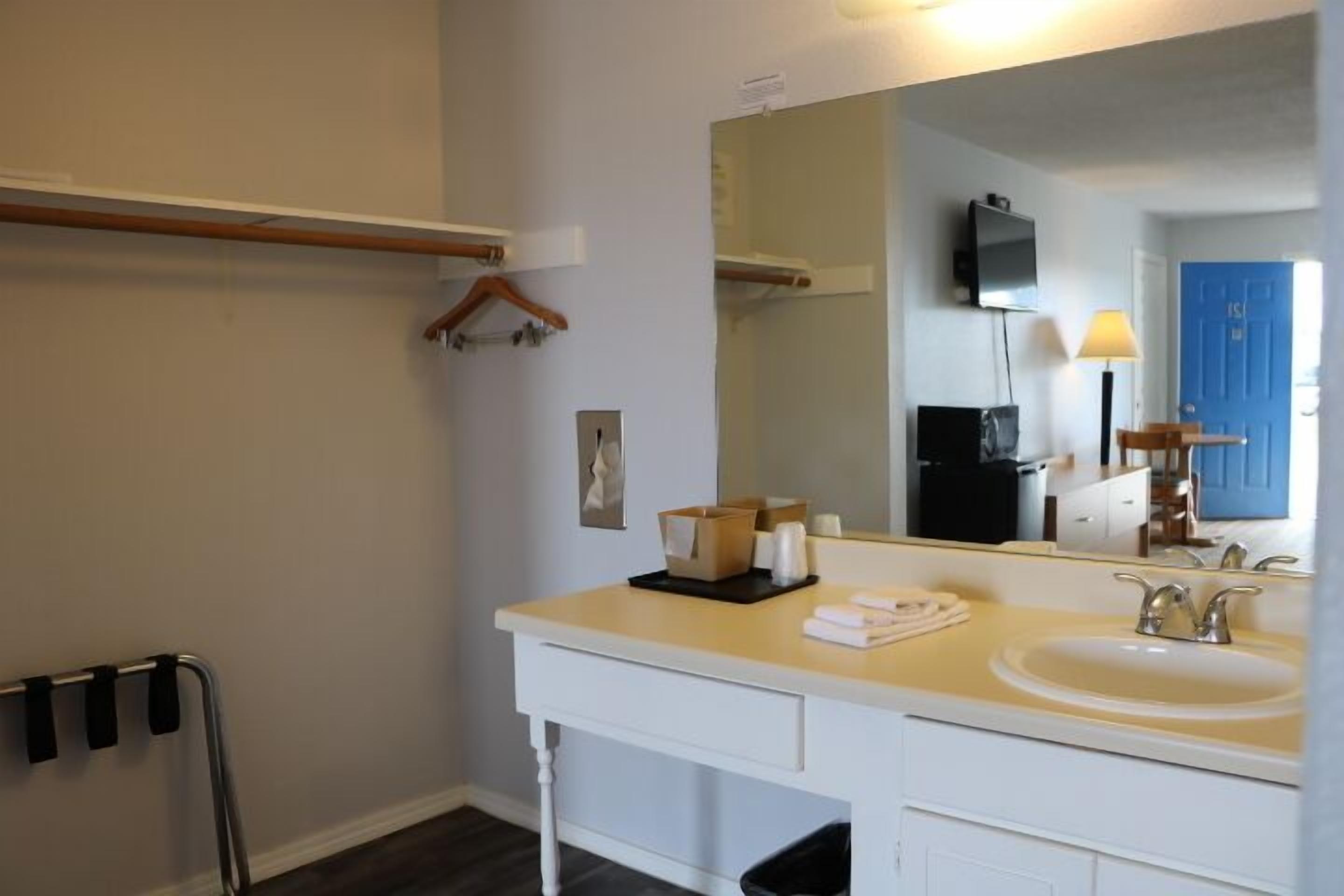 A bathroom with a white vanity, a large mirror, a sink, and a towel rack.