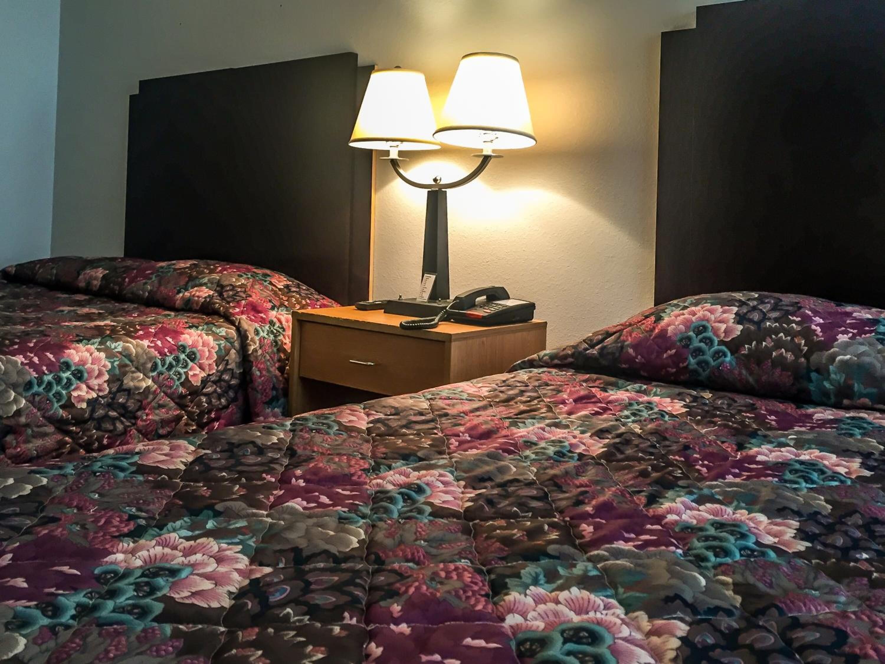 Habitación de hotel con dos camas, cada una con cubrecama estampado con motivos florales, una mesita de noche con lámpara y teléfono.