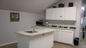 A compact kitchen with a central island, white cabinets, a microwave, and a coffee maker. - Bent Tree Motel (Emory)