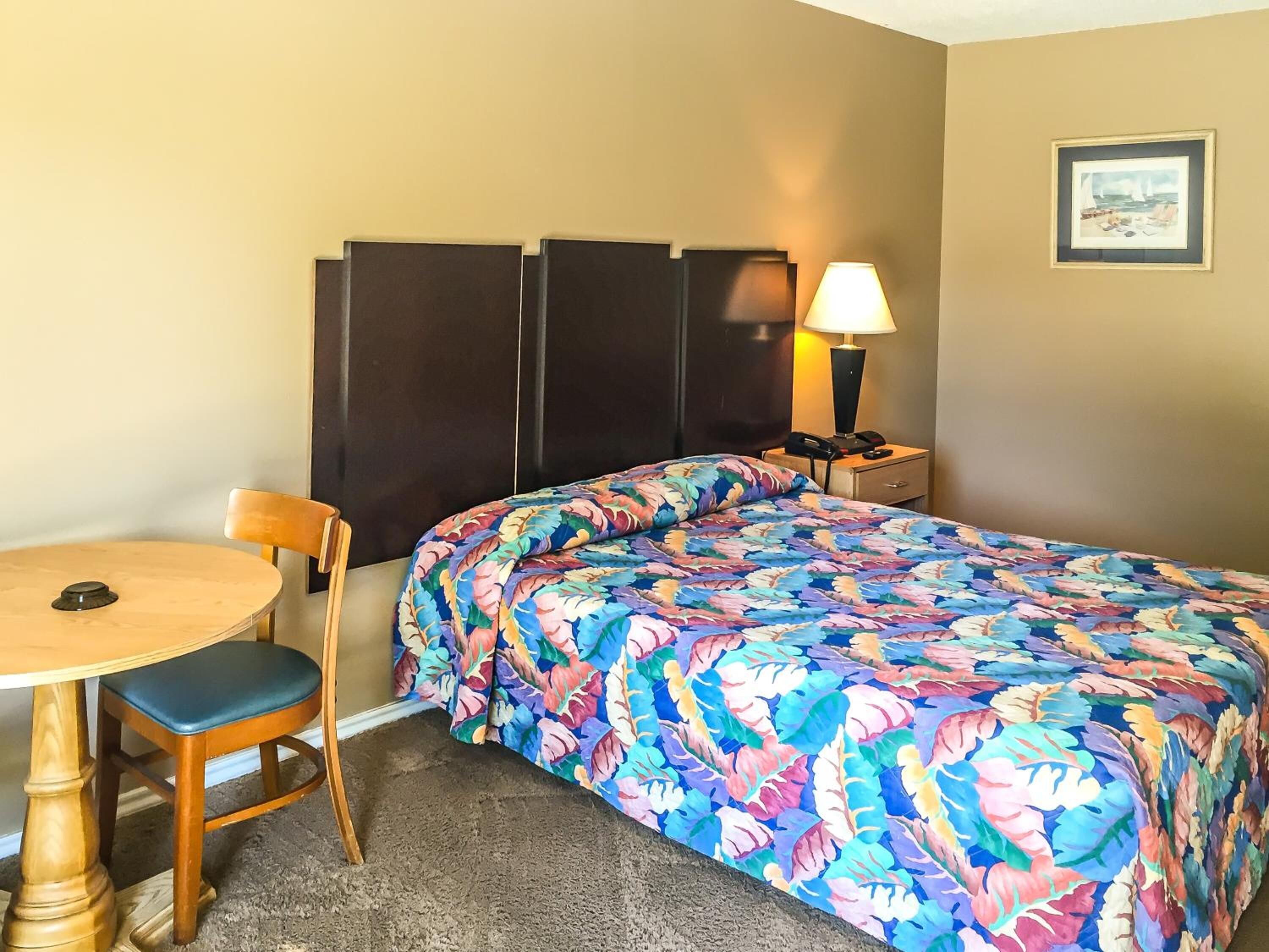 Una habitación de hotel con una cama, una silla, una mesa y una mesita de noche con lámpara.