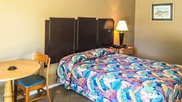 Una habitación de hotel con una cama, una silla, una mesa y una mesita de noche con lámpara.