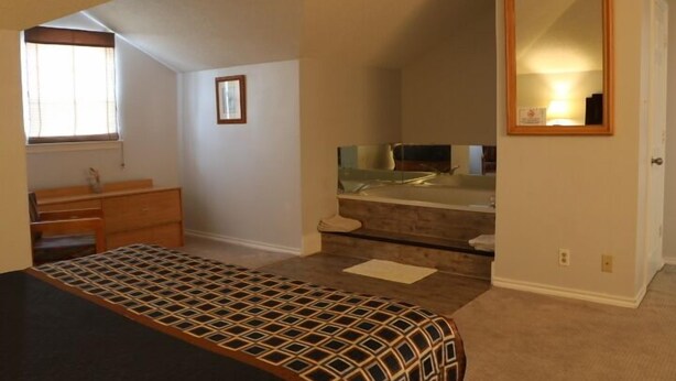 A bedroom with a bed, dresser, vanity, and a mirror. - Bent Tree Motel (Emory)
