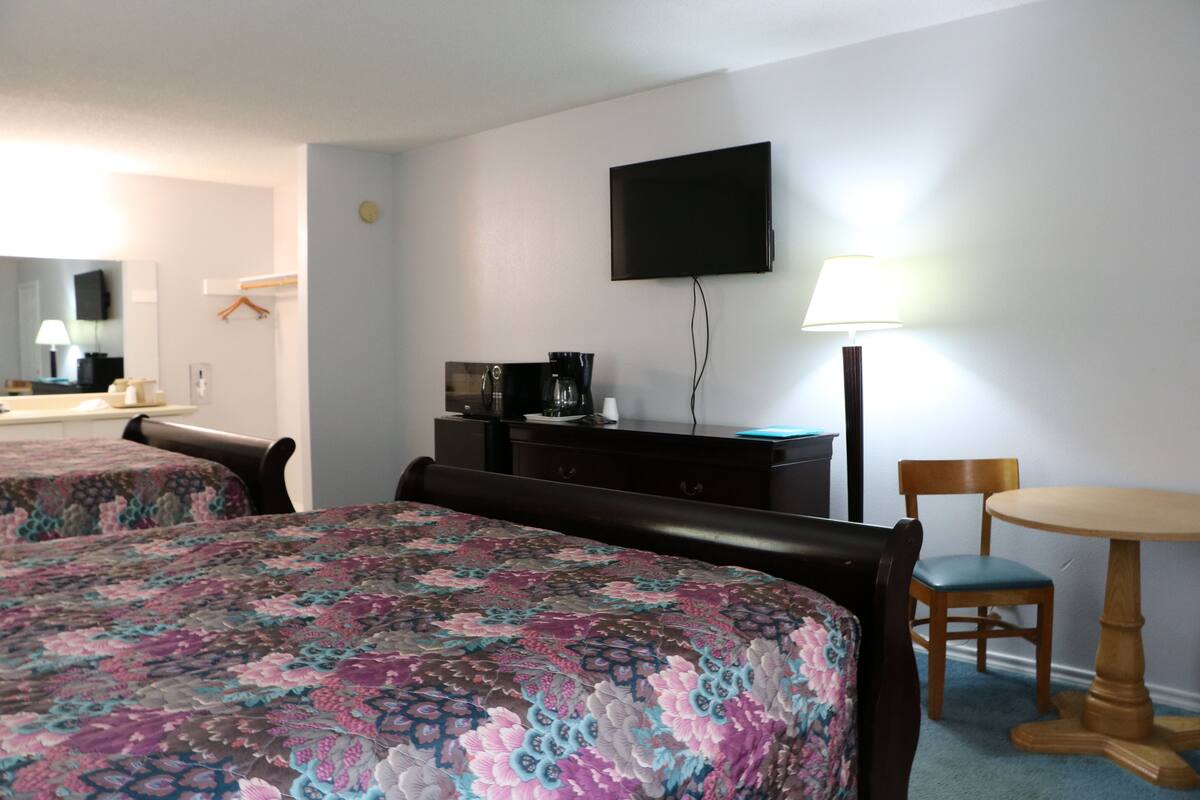 Habitación de hotel con dos camas, televisor, escritorio con lámpara y una silla.