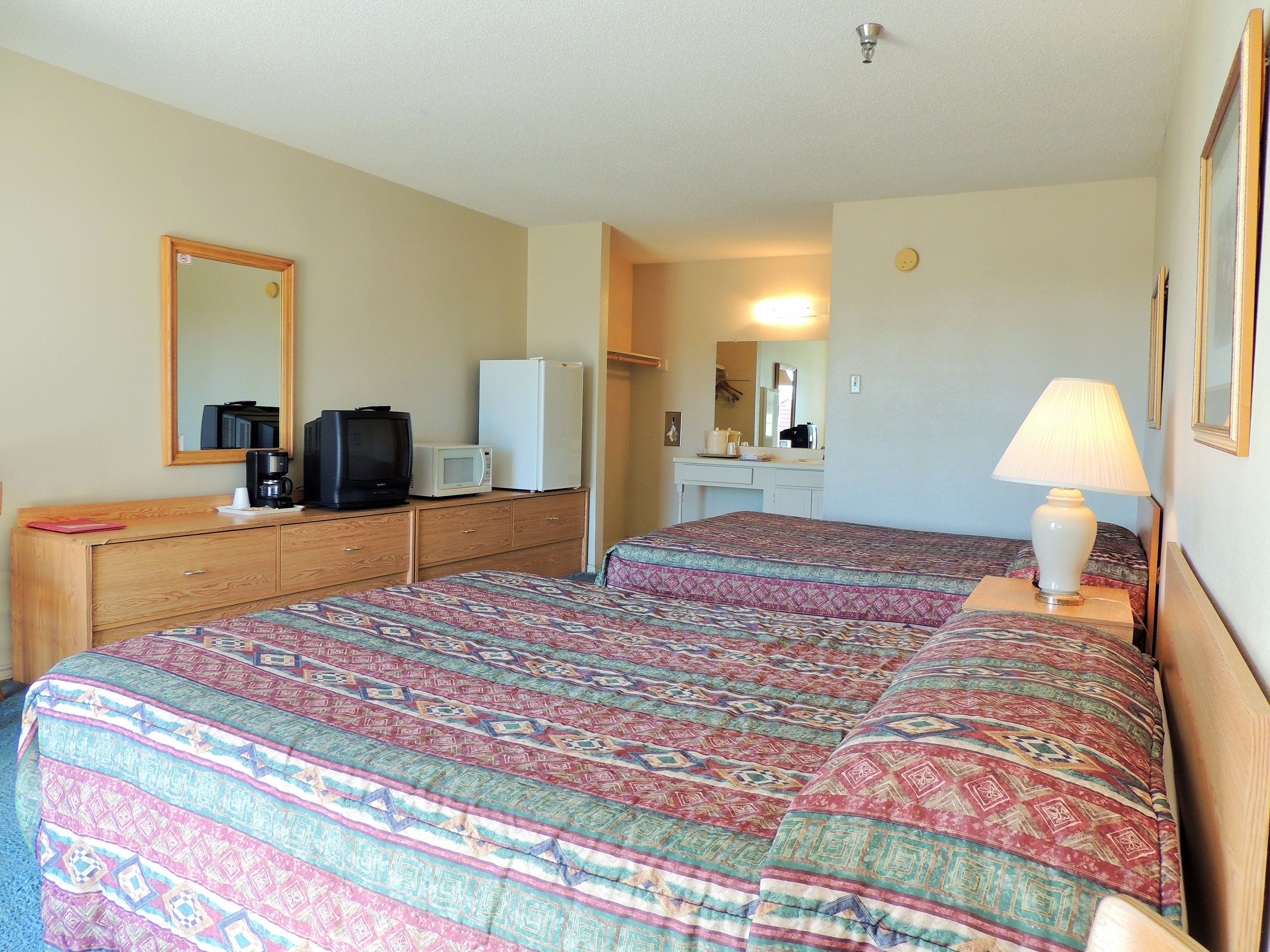 A hotel room with a bed, a dresser, a microwave, a refrigerator, a television, and a lamp.
