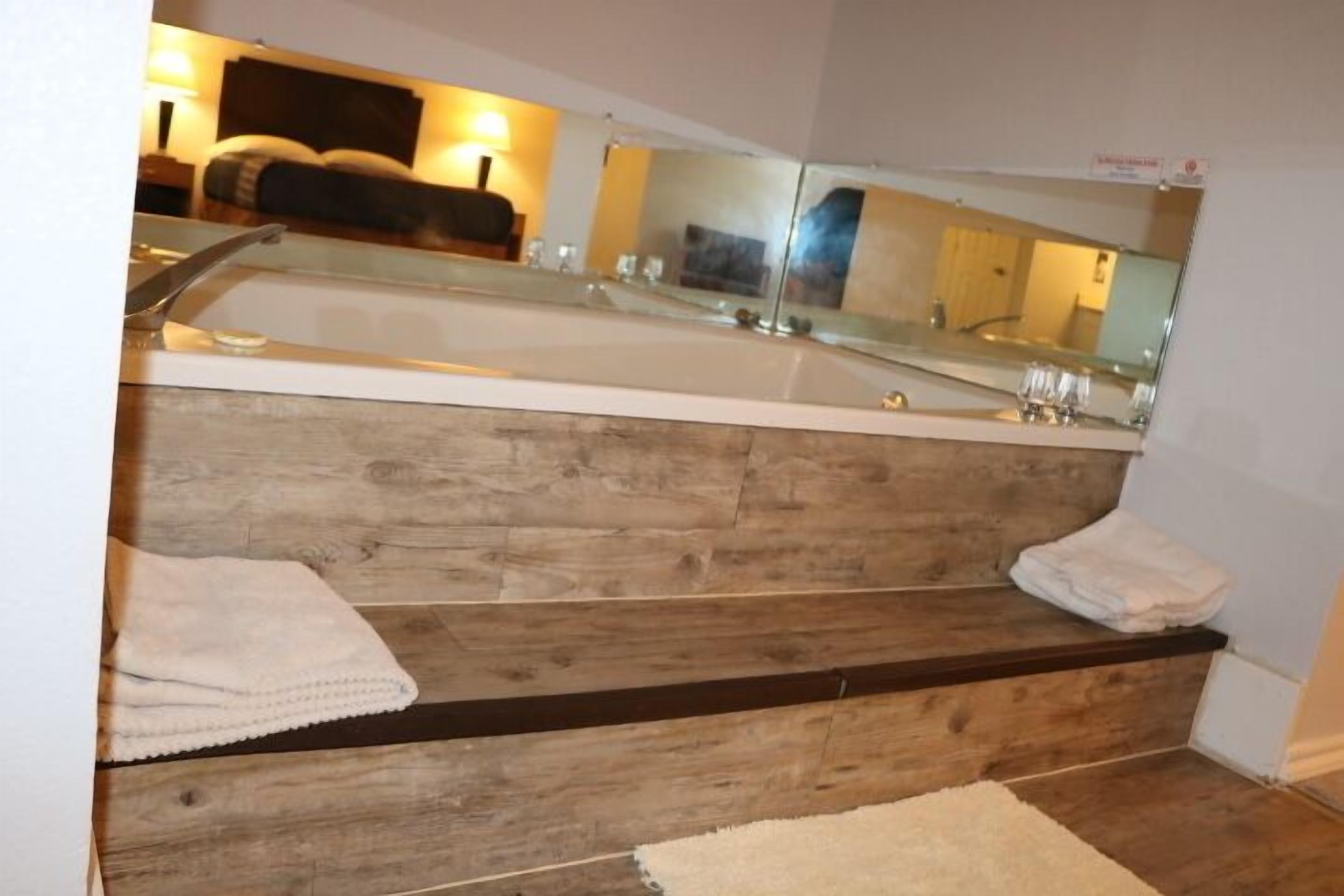 Un baño con un espejo grande, escalones de madera y una alfombra de baño blanca.