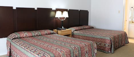 Een hotelkamer met twee enkele bedden, een nachtkastje met een lamp en een houten hoofdbord.