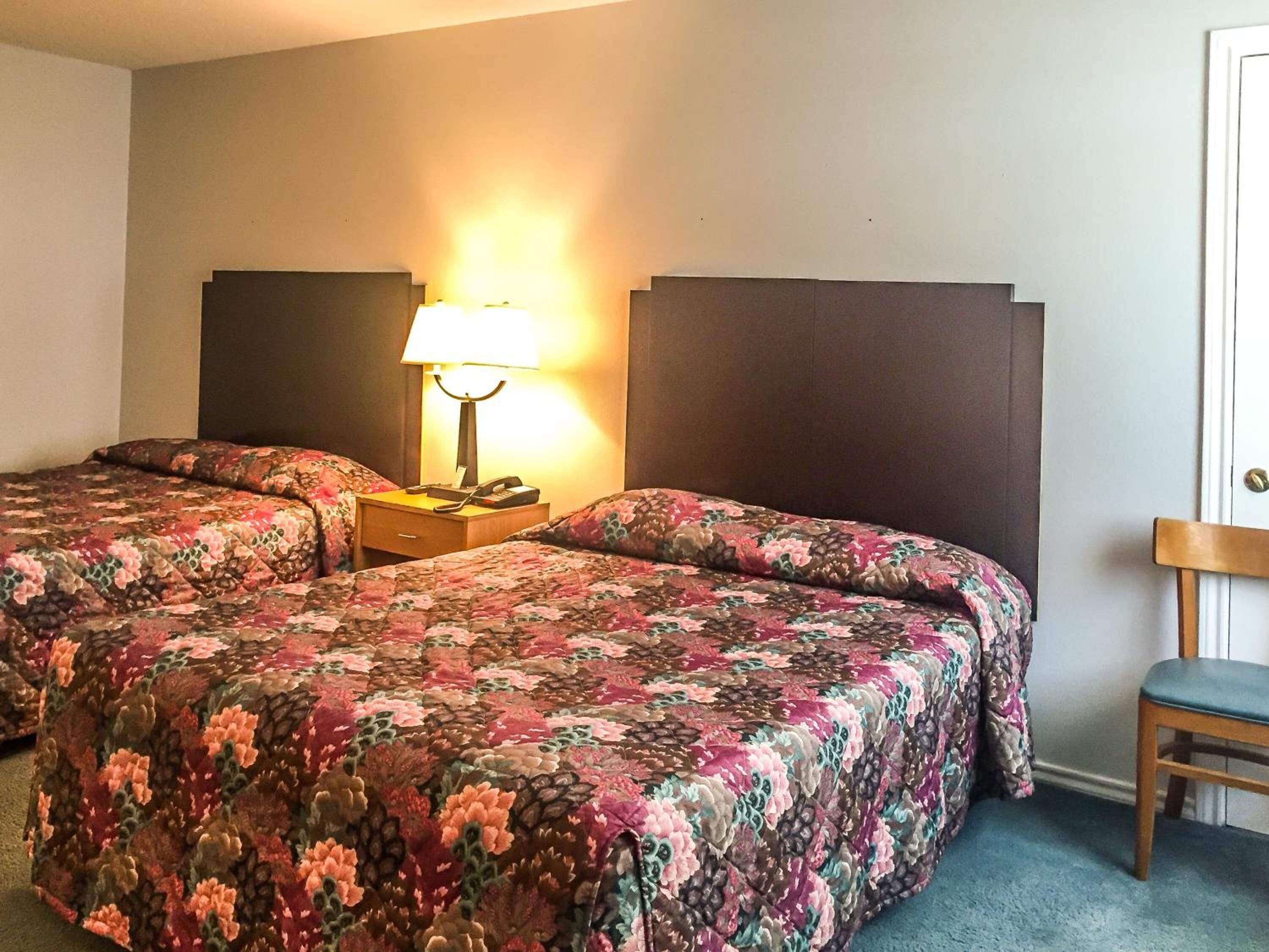 Une chambre d’hôtel avec deux lits, une table de chevet avec une lampe et une chaise.