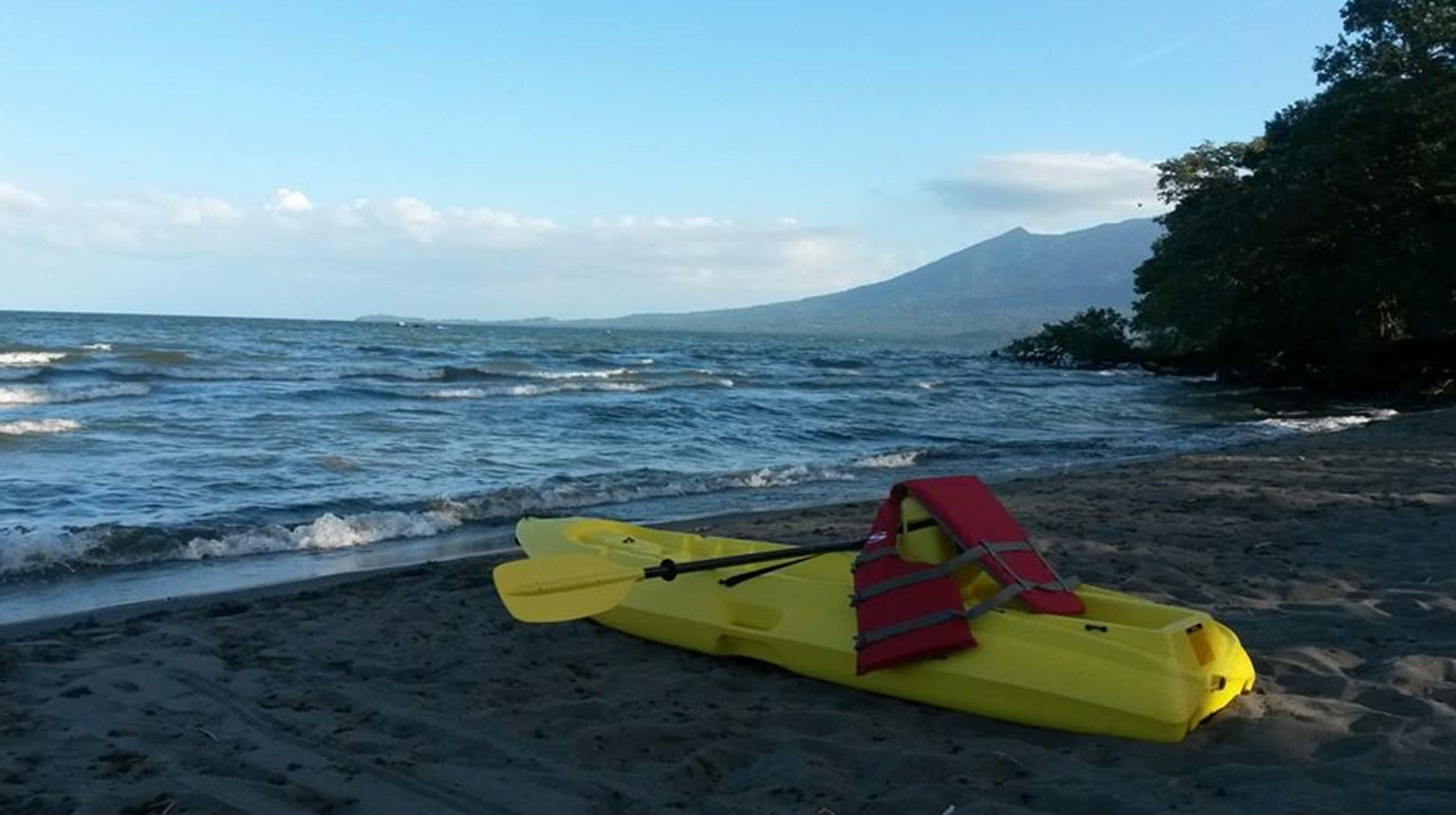 A kayak with a life jacket on a sandy beach with a mountain in the background.