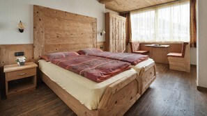 Ein Zimmer mit Holzboden, einem Bett, Nachttischen, einem Fenster mit Vorhängen und einem kleinen Tisch mit Stuhl.