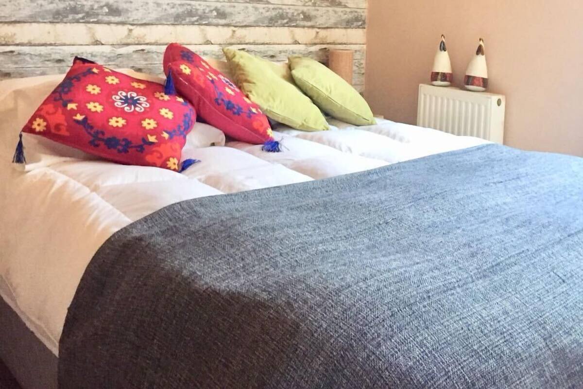 Un lit avec plusieurs oreillers, une tête de lit en bois, un radiateur et un petit élément de décoration murale.