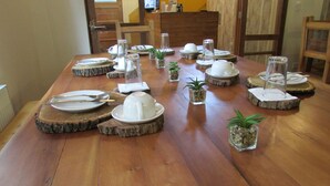 A wooden dining table set with white plates, cutlery, and glassware, surrounded by small potted plants. - Nativa Hotel Boutique (Santiago)