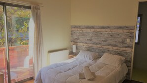 A bedroom with a bed, a wooden headboard, a window with a view of trees, and a door. - Nativa Hotel Boutique (Santiago)