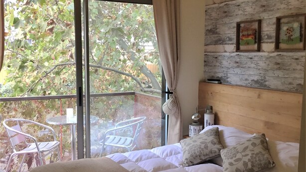 A bedroom with a bed, a window with a view of trees, a table with chairs outside, and a wooden wall with pictures. - Nativa Hotel Boutique (Santiago)