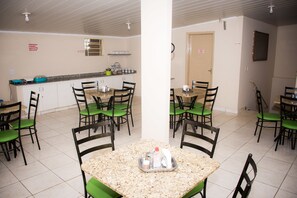 A dining area with multiple tables and chairs, a kitchen in the background, and a door with a sign. - Dok Brasília Hotel - Unidade Taguatinga (Águas Claras)