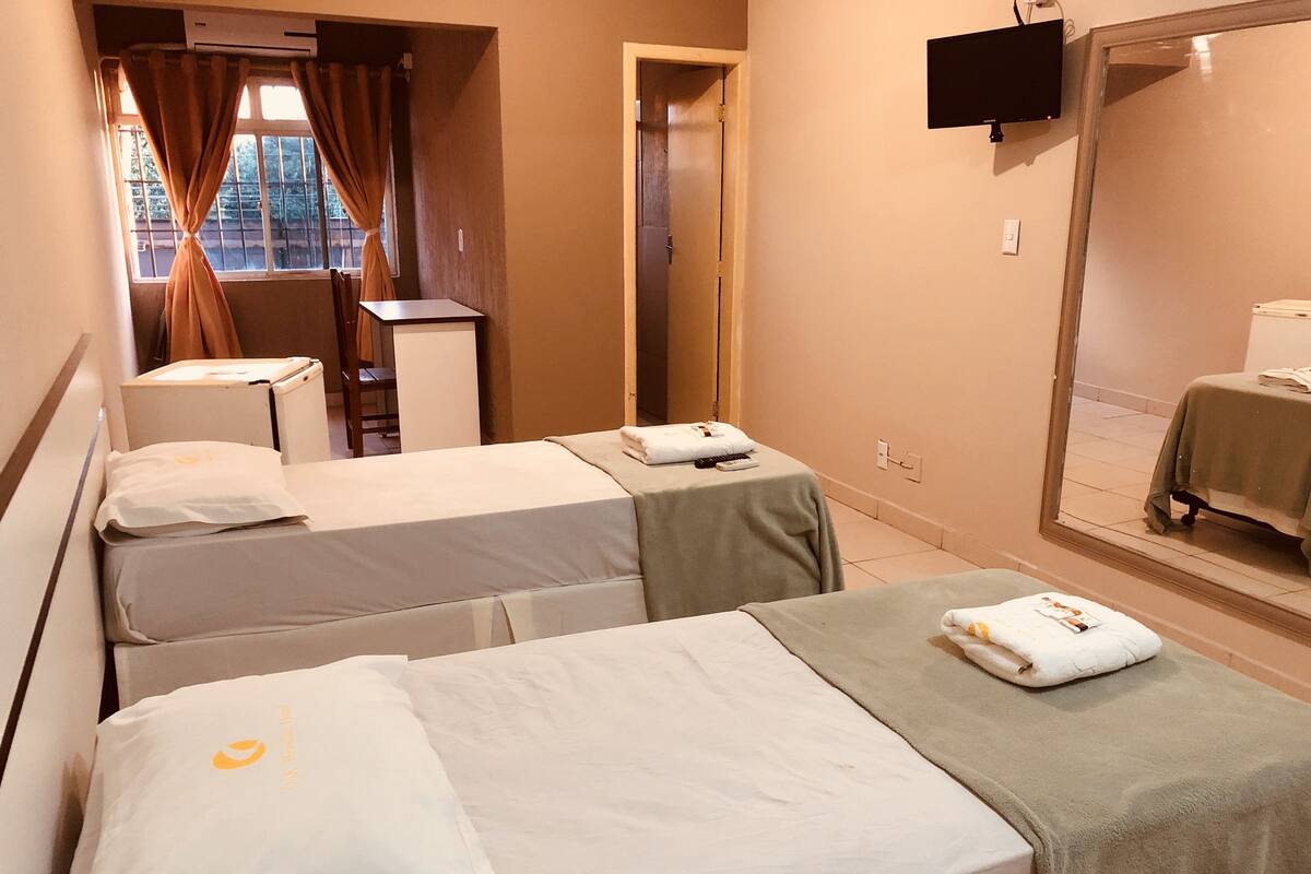 A hotel room with two single beds, a desk, a chair, a small table, and a TV mounted on the wall.
