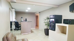 A reception area with a counter, a potted plant, a television, and a microwave. - Dok Brasília Hotel - Unidade Taguatinga (Águas Claras)