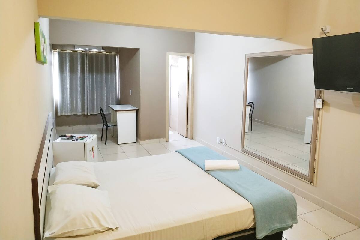 A hotel room with a bed, a desk, a chair, a television, and a bathroom mirror.
