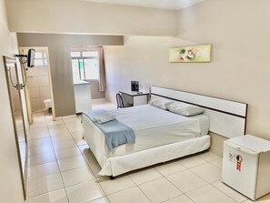 A bedroom with a bed, a bedside table, a small cabinet, and a window. - Dok Brasília Hotel - Unidade Taguatinga (Águas Claras)