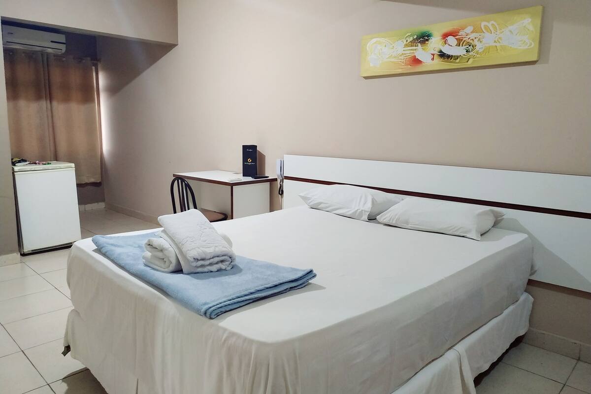 A hotel room with a bed, a desk, a chair, and a small refrigerator.