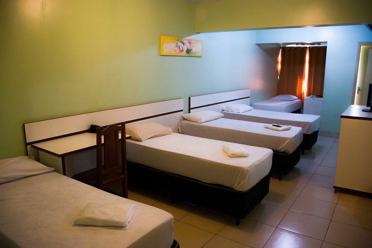 A hotel room with four single beds, a desk, a chair, and a small kitchenette.