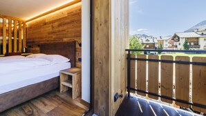 A wooden room with a bed, a small table, and a view of a mountain landscape. - Hotel Steinbock (Livigno)