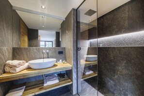 A modern bathroom with a large mirror, two sinks, wooden shelves, and a glass shower enclosure. - Hotel Steinbock (Livigno)
