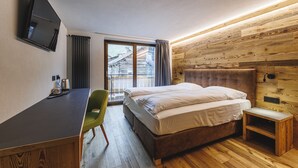 A hotel room with a bed, a desk, a chair, a television, and a window with curtains. - Hotel Steinbock (Livigno)