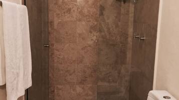 Un baño con ducha envuelta en vidrio, inodoro blanco y una toalla colgada en la pared.