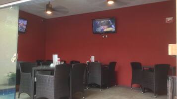 An indoor seating area with wicker chairs and tables, a television mounted on the wall, and a red wall.