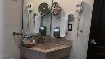 A bathroom with a sink, two mirrors, a hairdryer, a telephone, and a toilet.