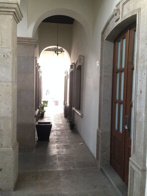 A corridor with a tiled floor, a wooden door with glass panels, and a hanging light fixture. - Hotel San Xavier (Querétaro)