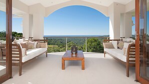 A balcony with a wooden table and two sofas, offering a view of the landscape. - Alexandria Retreat (Doonan)